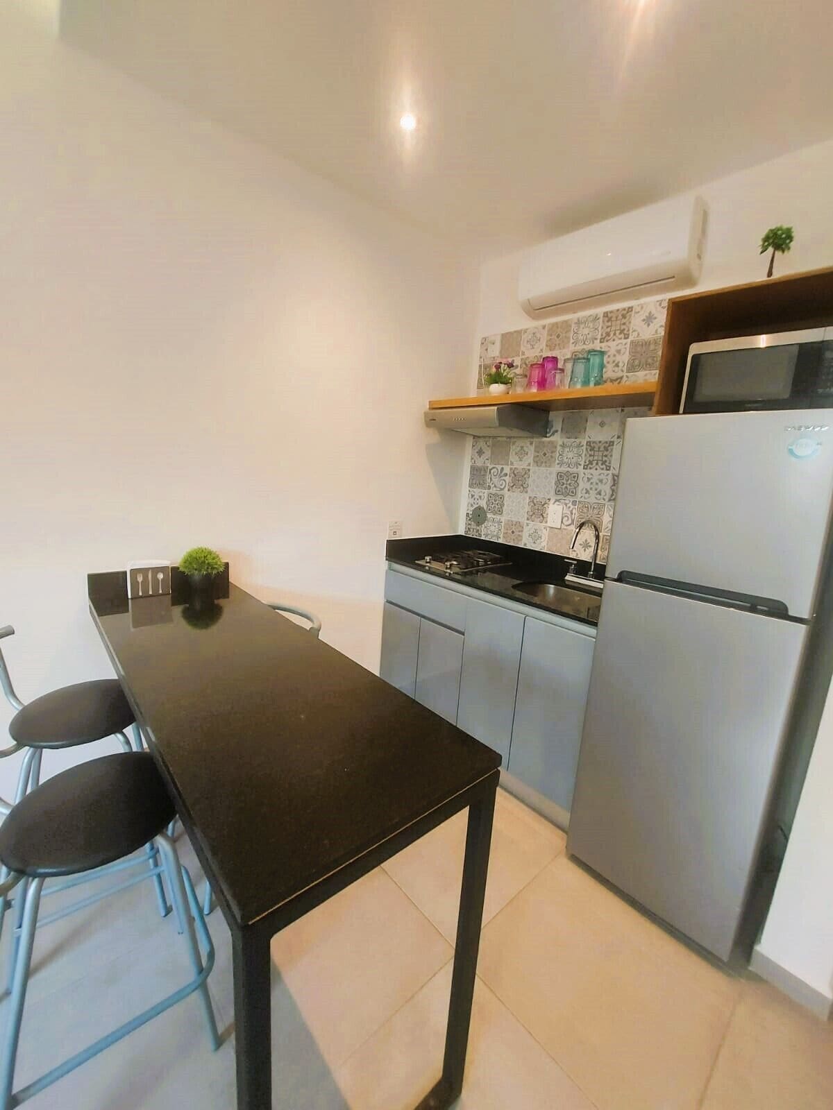 A compact kitchen with a black table, four chairs, a stove, a refrigerator, and a microwave.