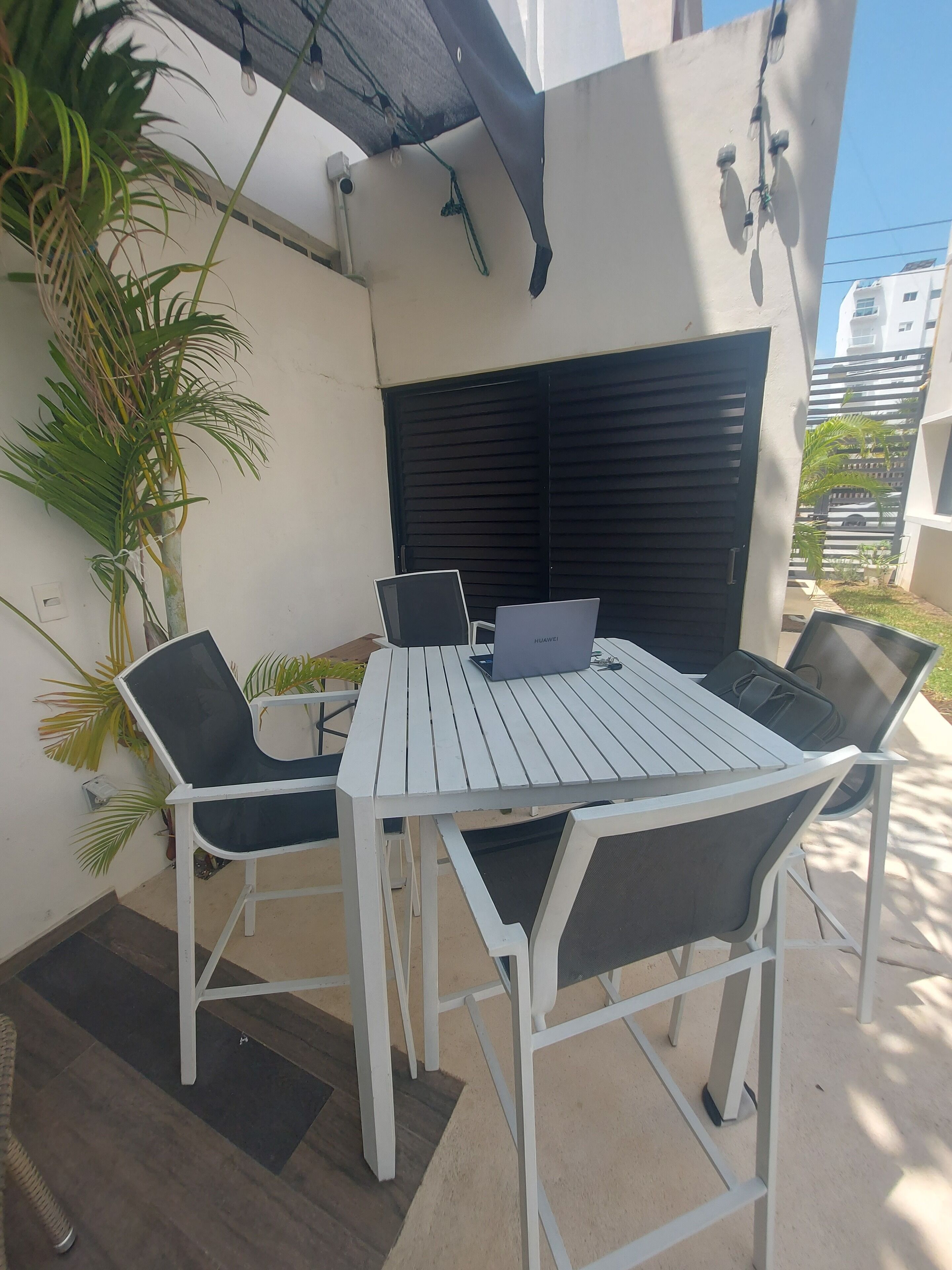 An outdoor patio with a white metal table and chairs, a laptop, and a smartphone.