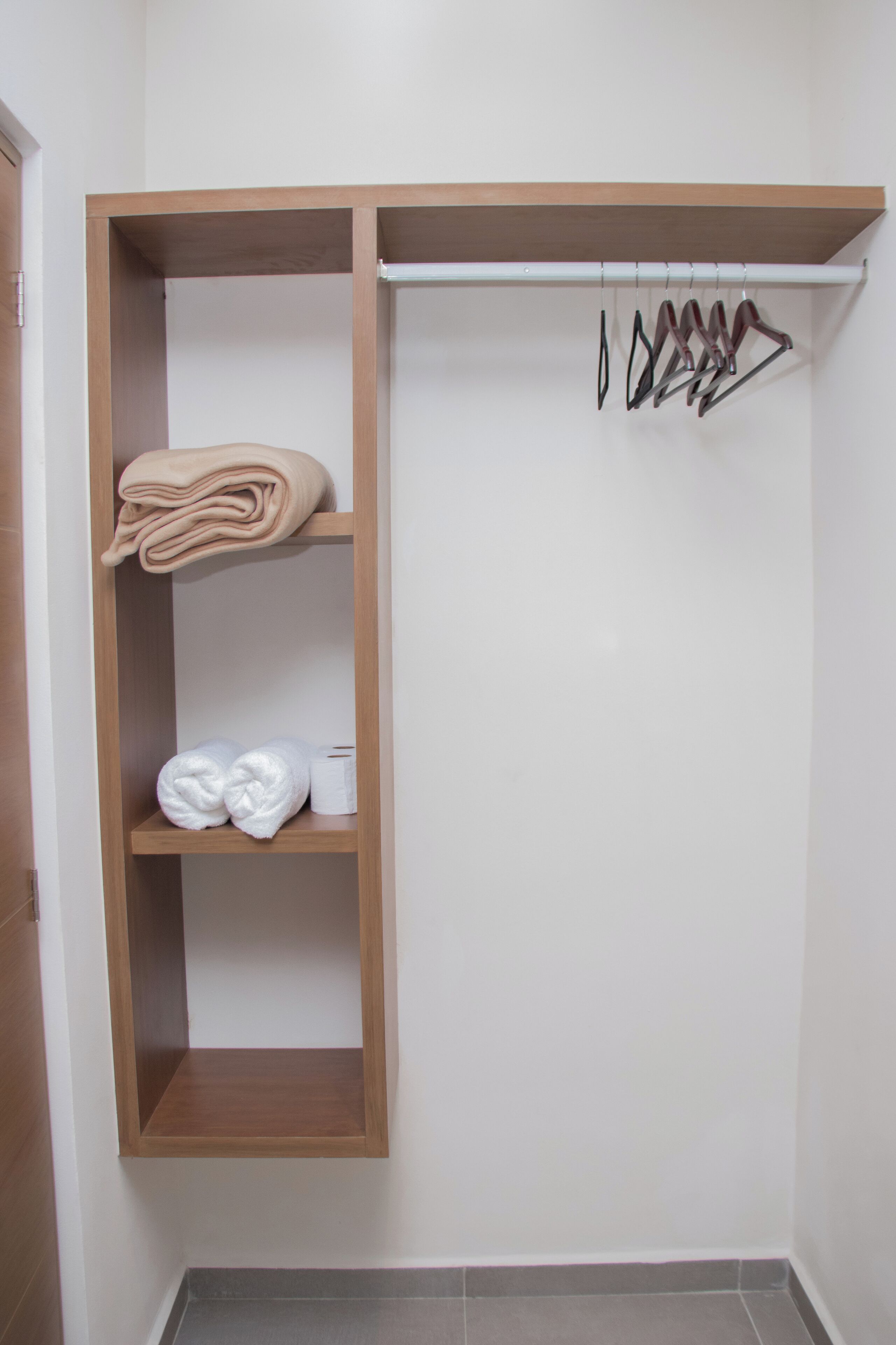 A wooden closet with shelves holding folded towels and a hanging rack with clothes.