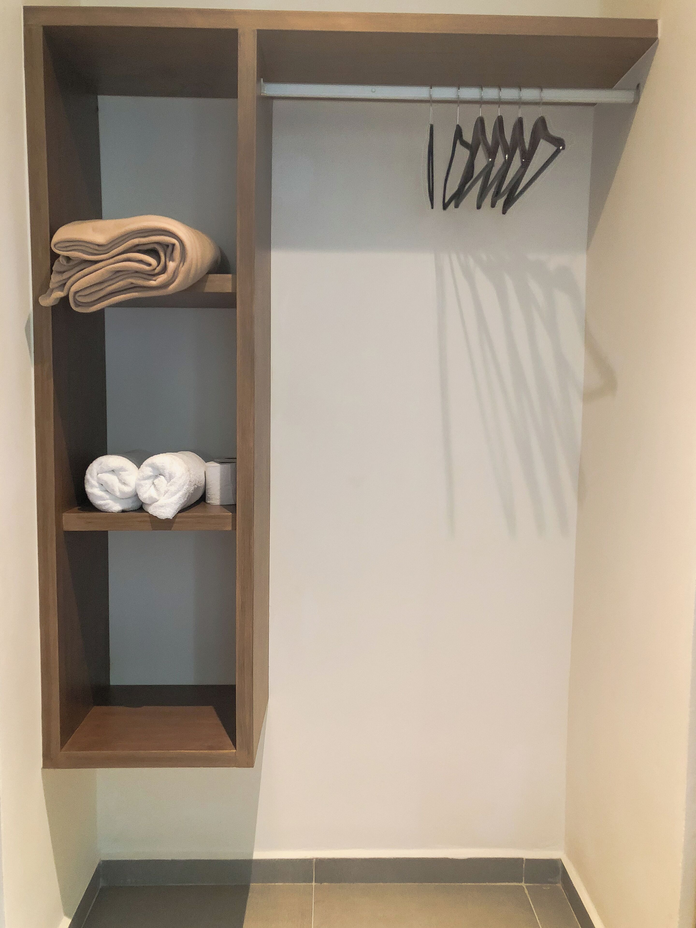 A corner of a room with a wooden shelf holding folded towels and a whiteboard with black writing.