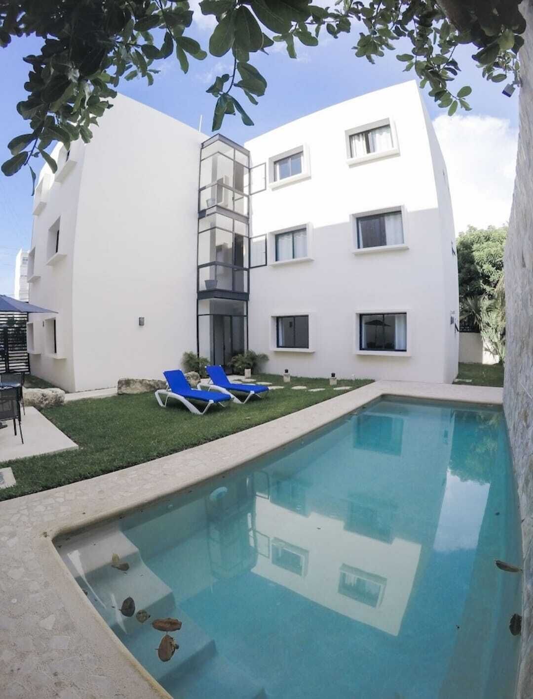 En moderne bygning med swimmingpool, blå liggestole og et lille haveområde.