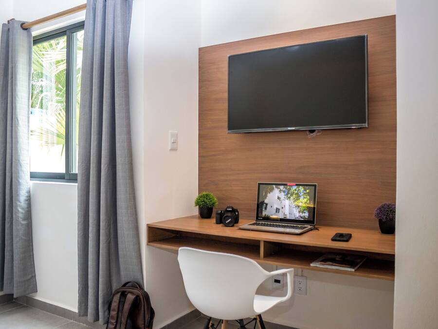 A modern room with a wooden desk, a mounted TV, a laptop, a camera, and a white chair.