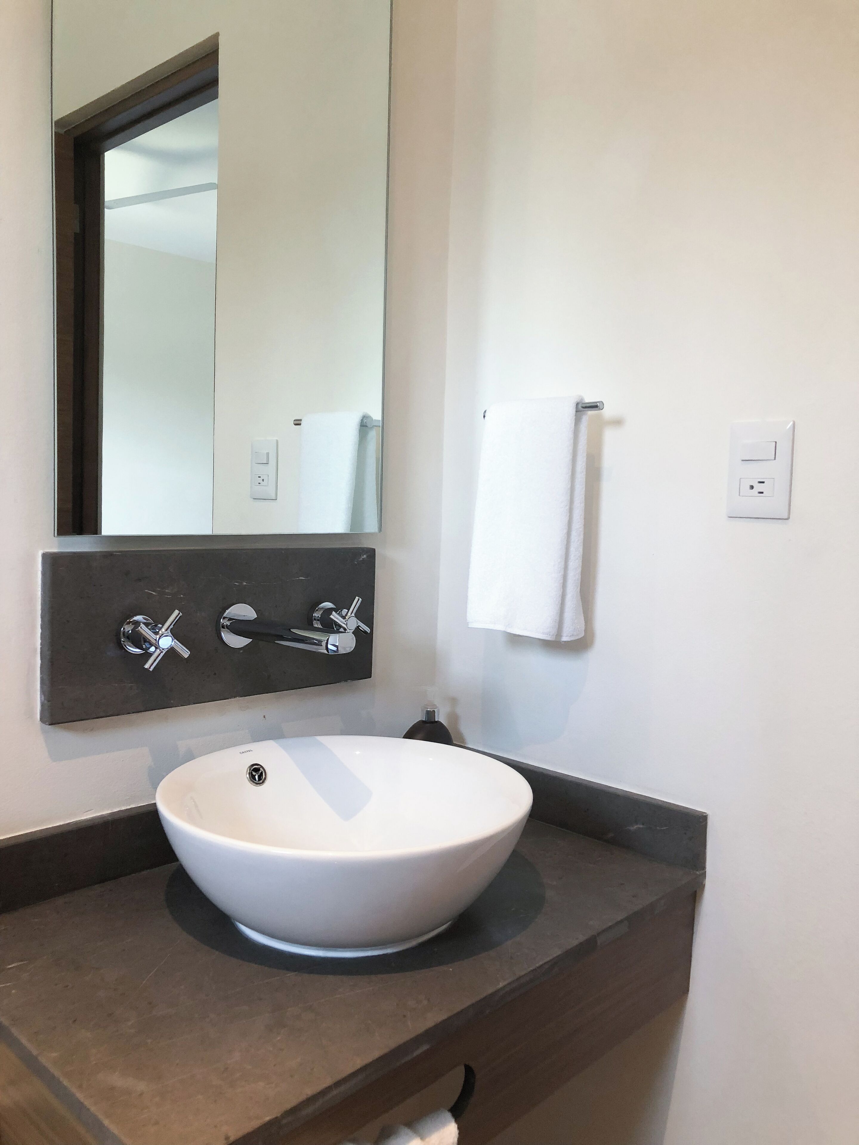 A bathroom with a white sink, a mirror, a towel rack, and a wall-mounted light switch.