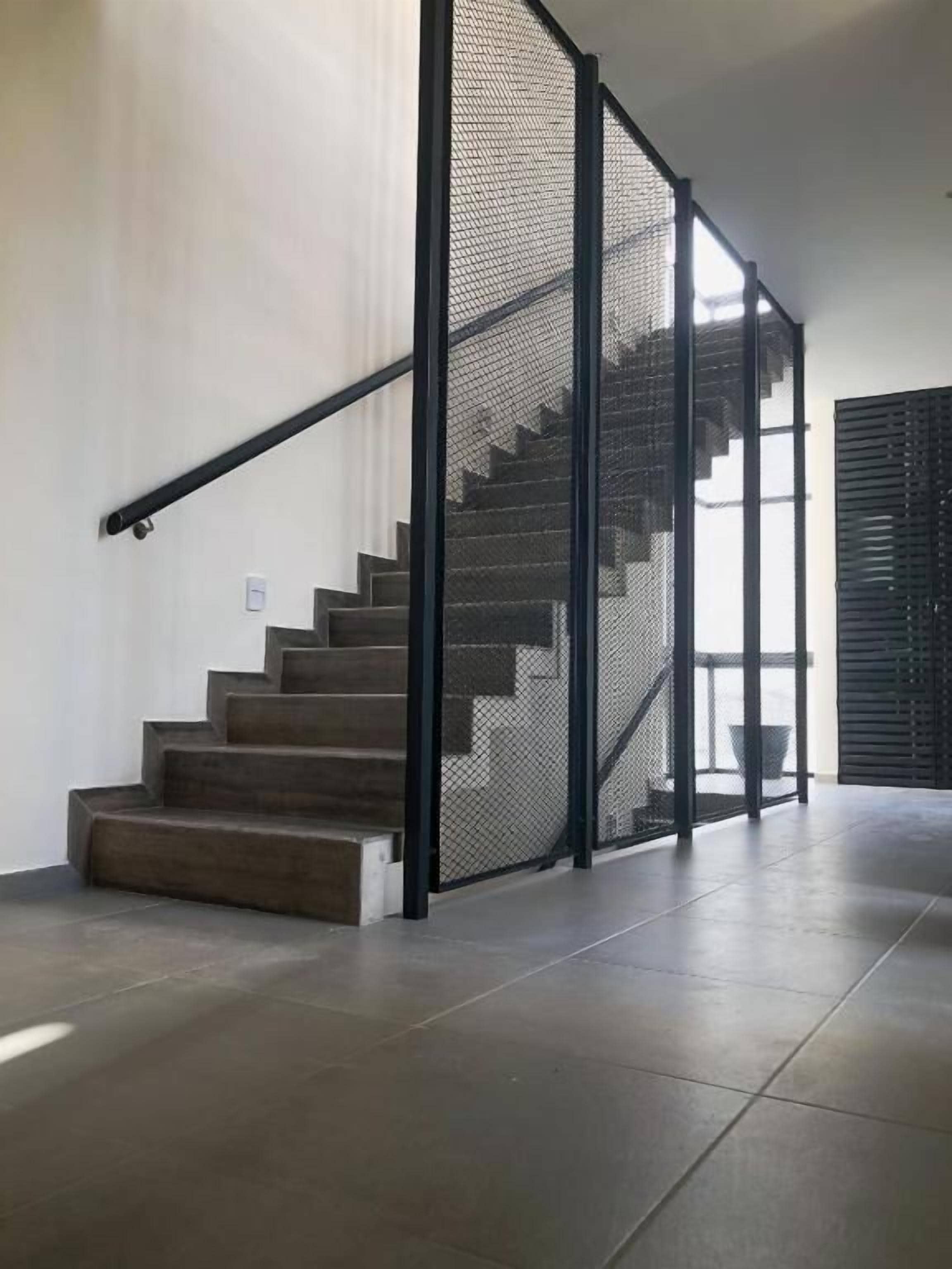 A staircase with a metal railing and a mesh screen, leading to a landing with a view of the outdoors.
