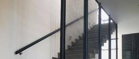 A staircase with a metal railing and a mesh screen, leading to a landing with a view of the outdoors.
