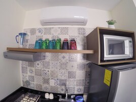 Una cocina con microondas, una estantería con botellas de agua de colores, cocina a gas y aire acondicionado de pared.