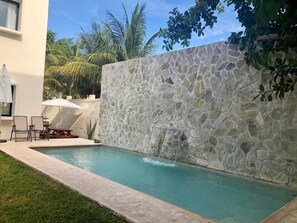 A swimming pool with a stone wall, a patio with chairs, and a palm tree in the background. - Viento Suites Cancún (Cancun)