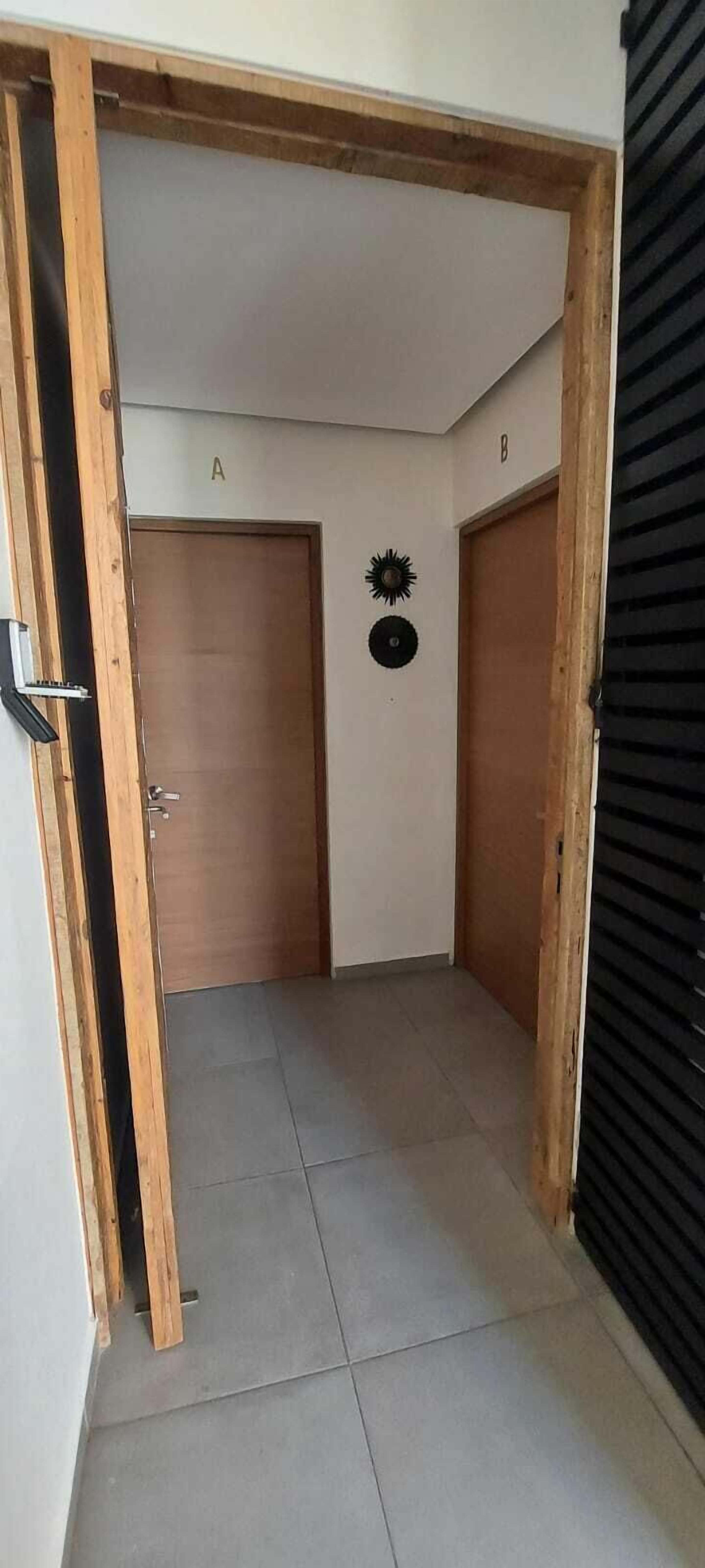 A hallway with two wooden doors labeled 'A' and 'B', a tiled floor, and a black shutter on the right.