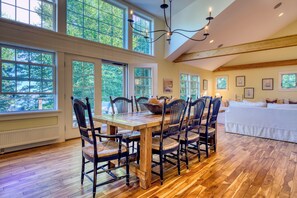 A dining area with a wooden table and chairs, large windows with a view of trees, and a chandelier.