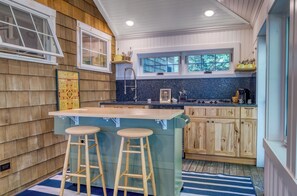 A kitchen with wooden cabinets, a central island with stools, and a window overlooking greenery.