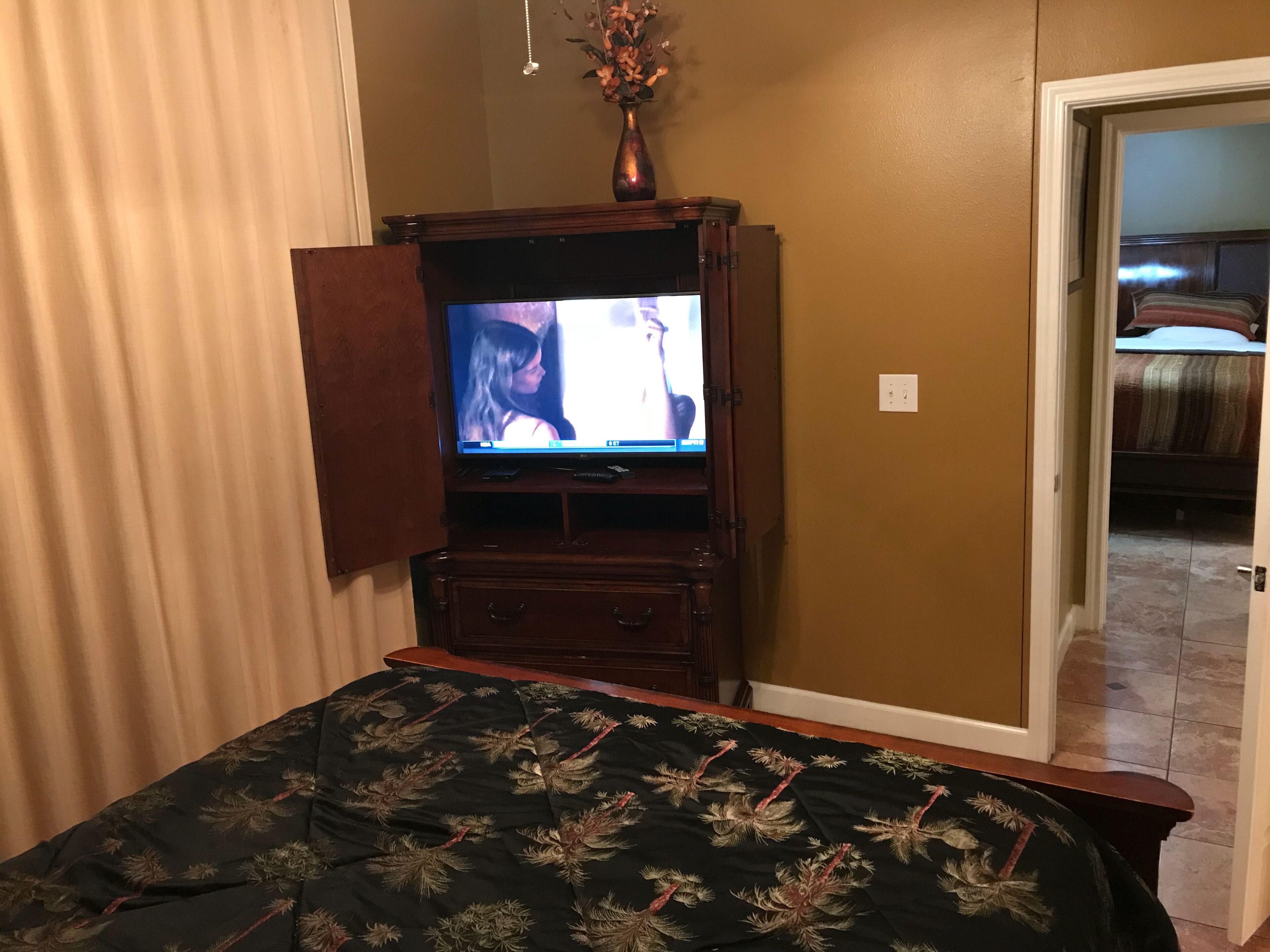 A bedroom with a bed, a television on a wooden stand, and a door leading to another room.