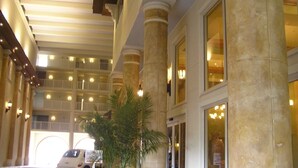 Un vestíbulo de hotel con techo alto, grandes columnas y una planta en maceta en el centro.