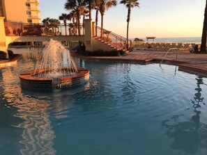 A pool with a central fountain, surrounded by palm trees and a bridge. - Luxury Beach Front Condo  (Panama City Beach)