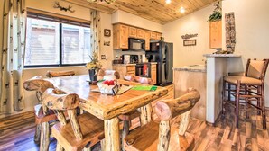 A rustic kitchen with wooden cabinets, a black refrigerator, and a dining table with carved wooden chairs. - 3 Mi to Fool Hollow Lake: Romantic Show Low Cabin (Show Low)