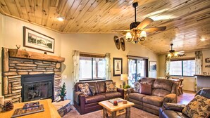 A cozy living room with a stone fireplace, leather sofas, a wooden coffee table, and a ceiling fan. - 3 Mi to Fool Hollow Lake: Romantic Show Low Cabin (Show Low)