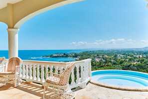 Un balcon avec des fauteuils en osier blanc et une piscine.