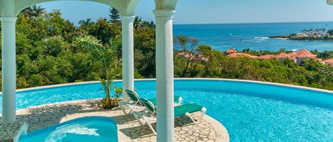 A pool with a view of the ocean and a tropical landscape.
