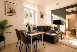 Uma sala de estar moderna com sofá, mesa de jantar com cadeiras, televisão e planta em vaso.