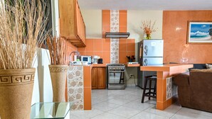 Una cocina con una isla central, estufa, microondas y refrigerador. Hay plantas decorativas y un cuadro en la pared.