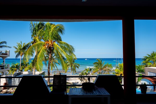 A balcony with a view of the beach, palm trees, and the ocean.