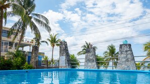Una piscina con vista despejada al océano, rodeada de palmeras y un edificio con balcones.