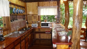 Une cuisine en bois avec un long comptoir, des casseroles suspendues, un four à micro-ondes et une fenêtre ornée de plantes.