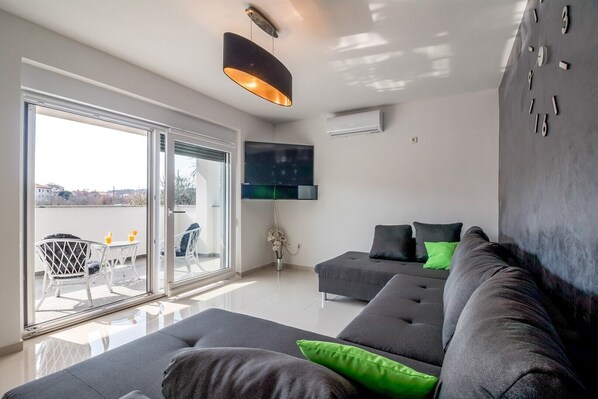 Relax in this stylish living room with a large sofa, flat-screen TV, and sliding glass door to an outdoor area.