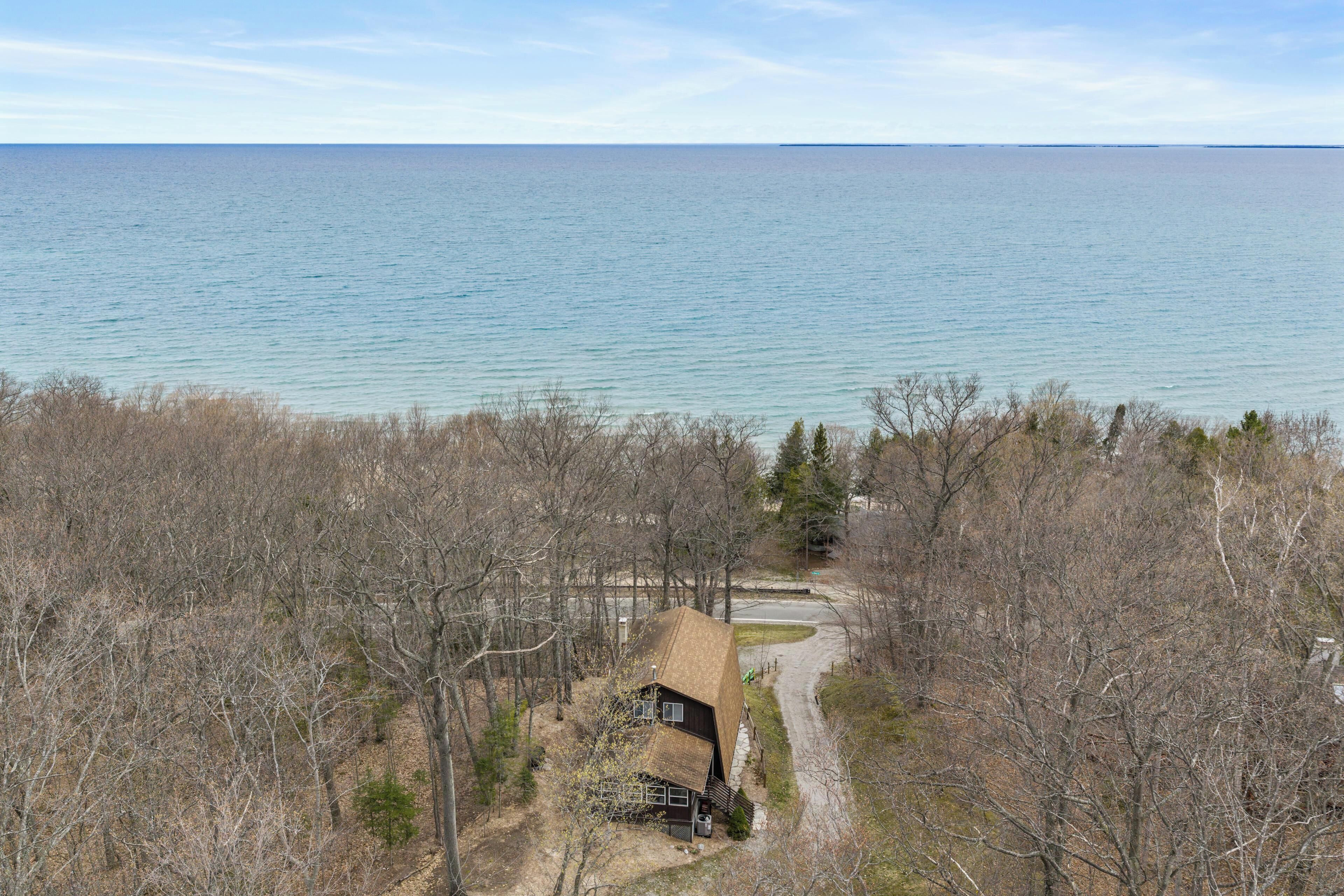 A cabin with a dirt path leading to it, surrounded by trees and overlooking a large body of water.