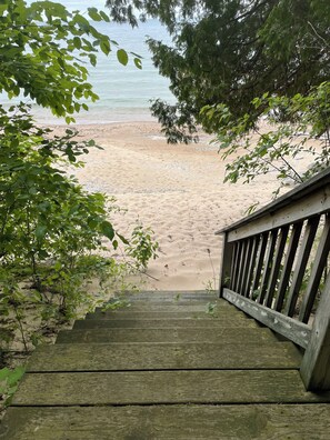 Un escalier en bois mène à une plage de sable, avec des arbres en premier plan.