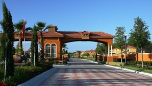 A street with a large archway, palm trees, and houses with red-tiled roofs.