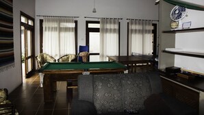A room with a pool table, a sofa, and a fan on a shelf. - Comfortable beach house with pool, terrace, barbecue, 300 m from the beach. (São Sebastião)