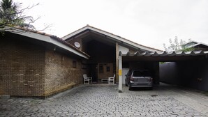 A building with a brick facade, a covered parking area, and a car parked inside. - Comfortable beach house with pool, terrace, barbecue, 300 m from the beach. (São Sebastião)