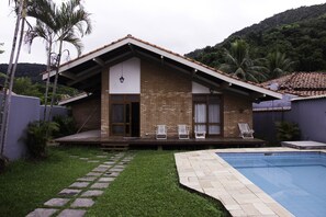 A house with a swimming pool, a patio with lounge chairs, and a brick exterior.