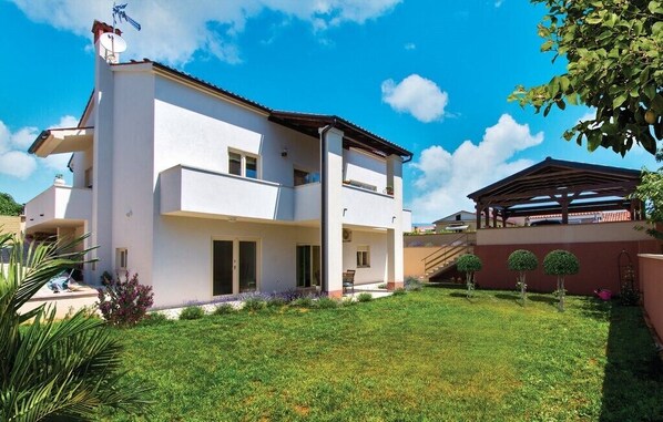 A two-story house with a flat roof, a balcony, and a covered patio area.