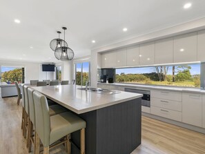 A modern kitchen with a large island, built-in appliances, and a view of the outdoors. - Bunya By The Sea - Absolute Beach Front  - Luxury Accommodation - Ocean Views (Cape Woolamai)