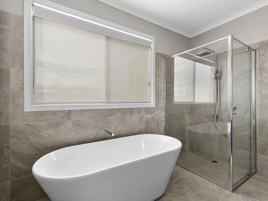 A modern bathroom with a freestanding bathtub, a glass shower enclosure, and a large window above the bathtub.
