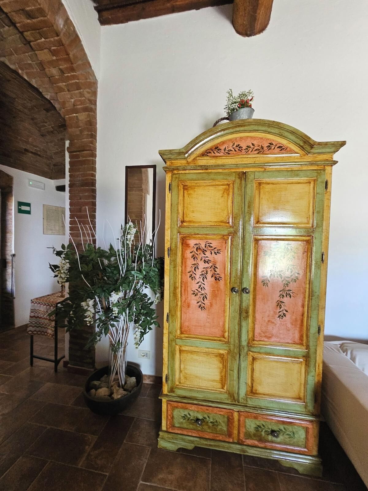 Una habitación con un mueble de madera grande con detalles florales, una planta en maceta y piso de baldosas.