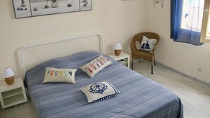 A neatly arranged bedroom with a bed, pillows, a chair, a nightstand, a lamp, and a wall-mounted picture. - House / Villa - Frontignan (Frontignan)
