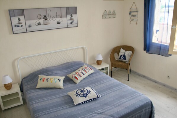 A neatly arranged bedroom with a bed, pillows, a chair, a nightstand, a lamp, and a wall-mounted picture. - House / Villa - Frontignan (Frontignan)