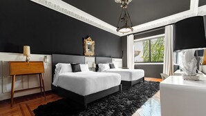 Een moderne slaapkamer met twee bedden, een groot zwart vloerkleed, houten vloeren en een groot raam met uitzicht op groen.