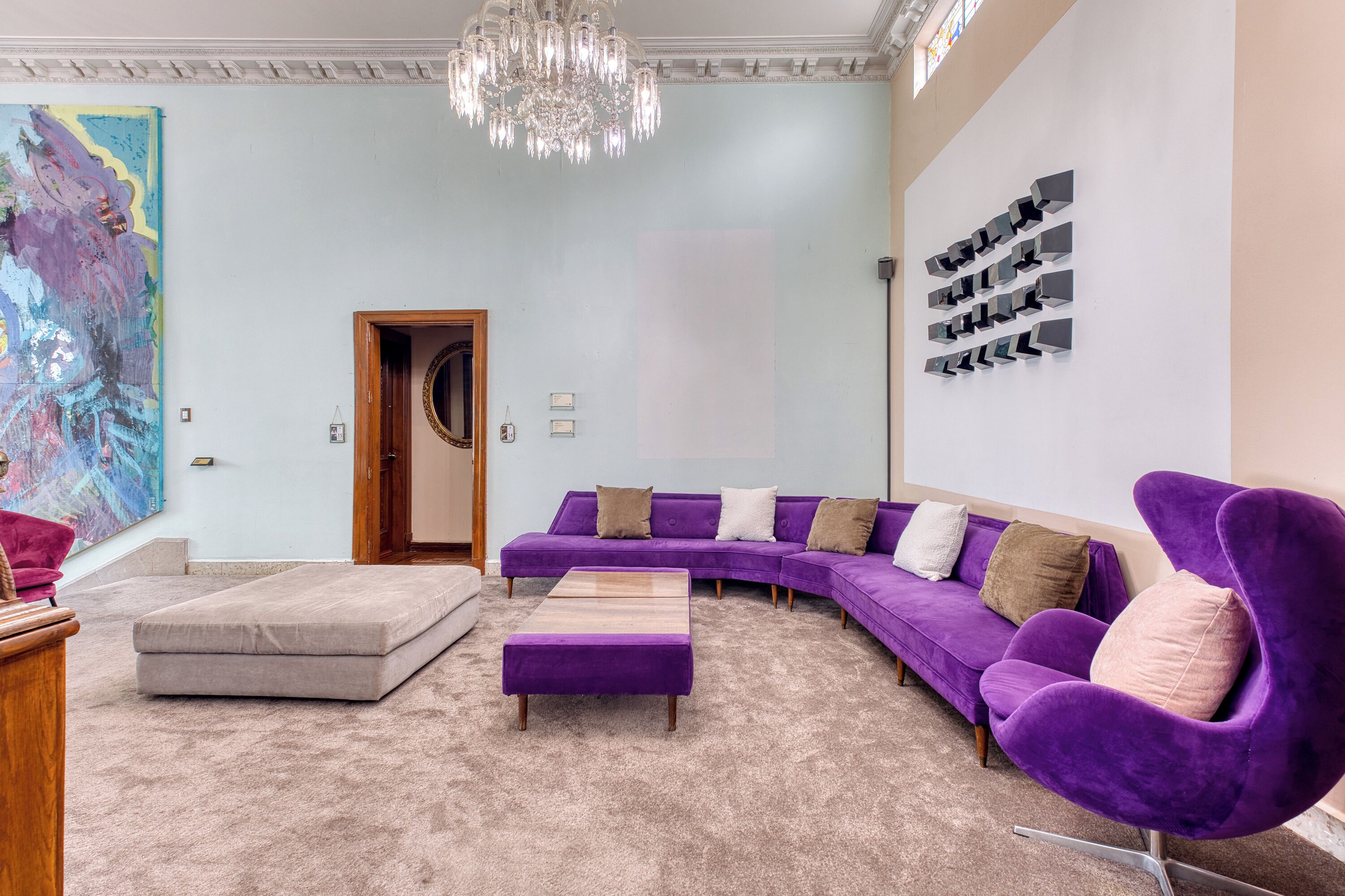A modern living room with a sectional sofa, a purple armchair, a wooden coffee table, and a large abstract painting on the wall.