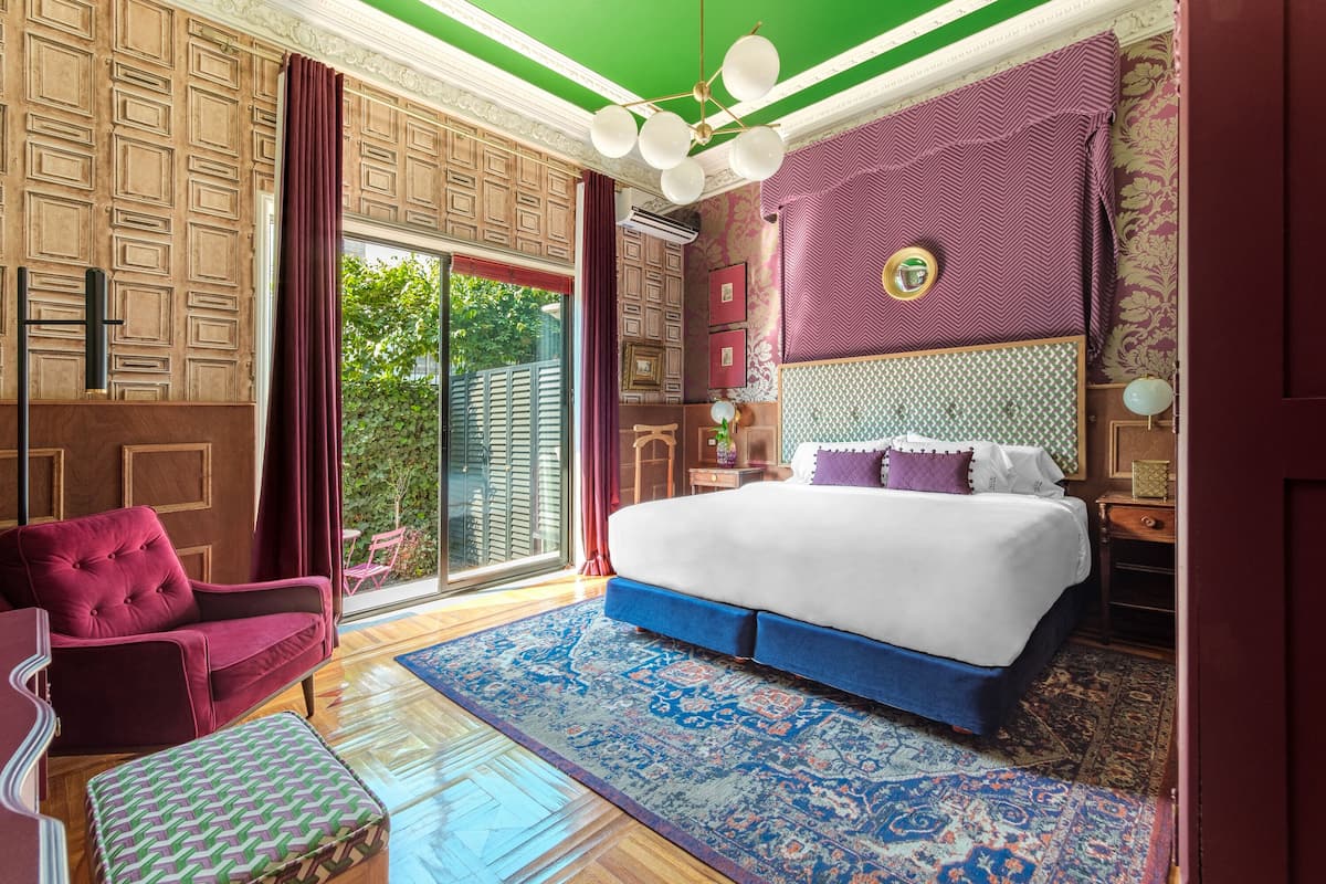Une chambre avec un grand lit, un canapé rouge, un tapis à motifs et une vue sur la verdure à l’extérieur.