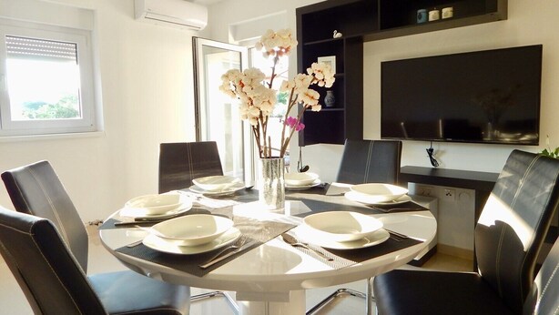 A dining area with a round table set for four, surrounded by black leather chairs. A vase with white flowers is on the table. - Comfortable holiday house with apartments / Beautiful first floor apartment with terrace and grill / A3 (Pula)