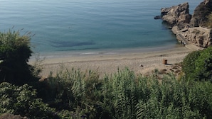 A coastal beach with rocky cliffs and a clear view of the sea.