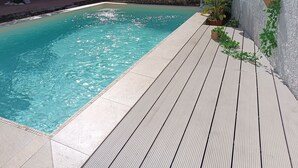 A rectangular swimming pool with clear blue water, surrounded by a wooden deck and a tiled walkway. - Typical house in finely furnished Sicilian style (Riposto)
