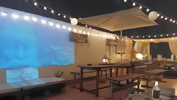 An outdoor seating area with tables and benches, string lights, and a projection screen displaying a landscape. - Typical house in finely furnished Sicilian style (Riposto)
