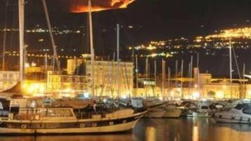 Una marina di notte, con barche ormeggiate e un fuoco visibile in lontananza.