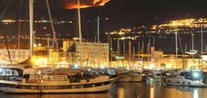 A marina at night with boats docked and a fire visible in the distance. - Typical house in finely furnished Sicilian style (Riposto)