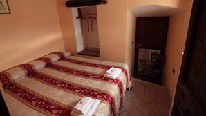 Quarto de hotel com uma cama, porta de madeira e um pequeno corredor.