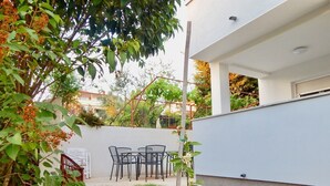 Un patio exterior moderno con un muro blanco, una pequeña zona con césped y una mesa con sillas.